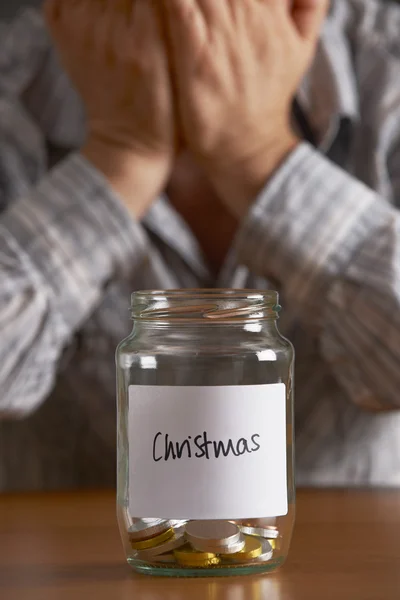 Hombre con la cabeza en las manos mirando tarro etiquetado Navidad — Foto de Stock