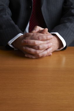 Katlanmış ellerle masada oturan işadamı