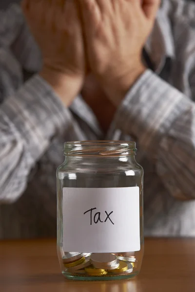 Mann mit dem Kopf in der Hand schaut auf Glas mit der Aufschrift Steuer — Stockfoto