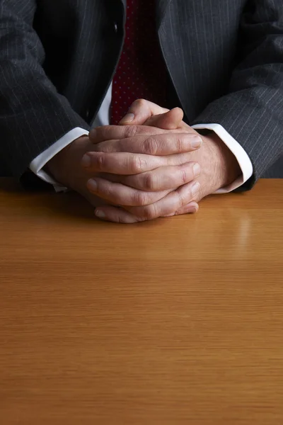 Affärsman som sitter vid skrivbord med knäppta händer — Stockfoto