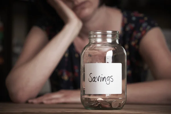 Mujer deprimida mirando frasco vacío etiquetado ahorros — Foto de Stock
