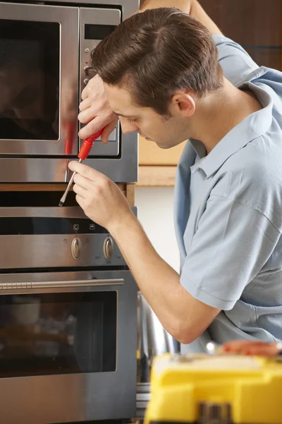 Мужчина ремонтирует домашнюю духовку на кухне — стоковое фото