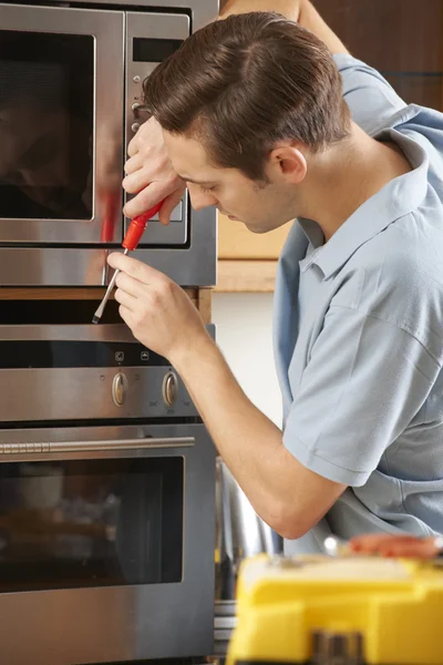 Homem que repara o forno doméstico na cozinha — Fotografia de Stock