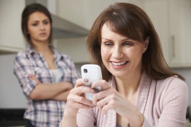Mother Texts On Mobile Phone As Daughter Watches In Background clipart