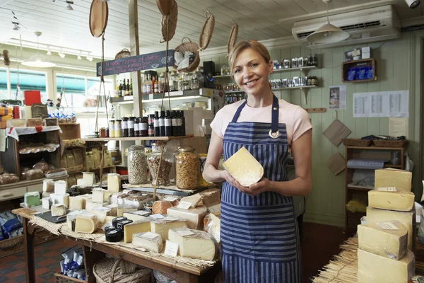 Ägare av delikatesser står i butiken håller ost — Stockfoto