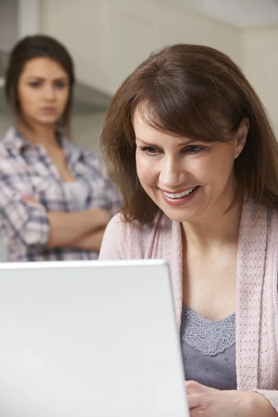 Mother Using Laptop With Frustrated Teenage Daughter In Backgrou — Stock Photo, Image