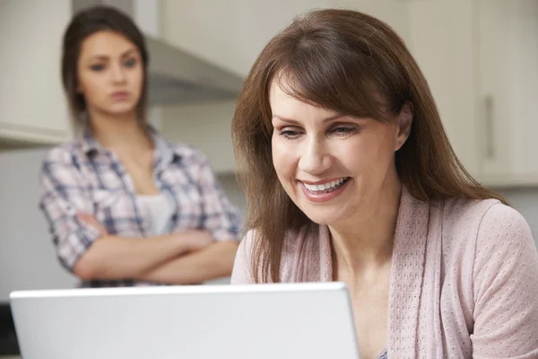 Mother Using Laptop With Unhappy Teenage Daughter In Background — Stock Photo, Image