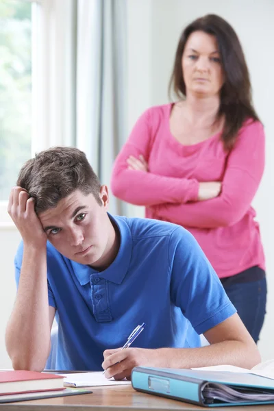 Разочарованная мать, смотрящая, как сын выполняет домашнюю работу — стоковое фото