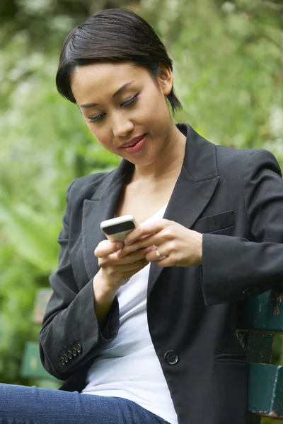 Junge Frau sitzt auf Bank und liest SMS — Stockfoto