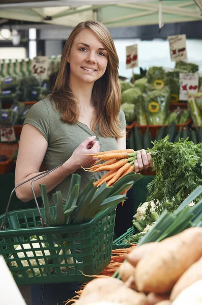 Mujer comprando zanahorias en puesto de verduras en el mercado — Foto de Stock