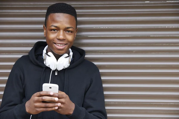 Мальчик-подросток слушает музыку и использует телефон в городских настройках — стоковое фото