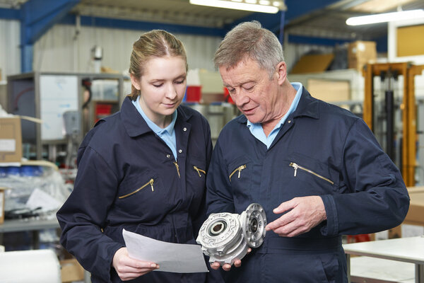 Engineer With Apprentice Looking At Component In Factory