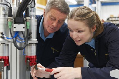 Engineer And Apprentice Working On Machine In Factory clipart