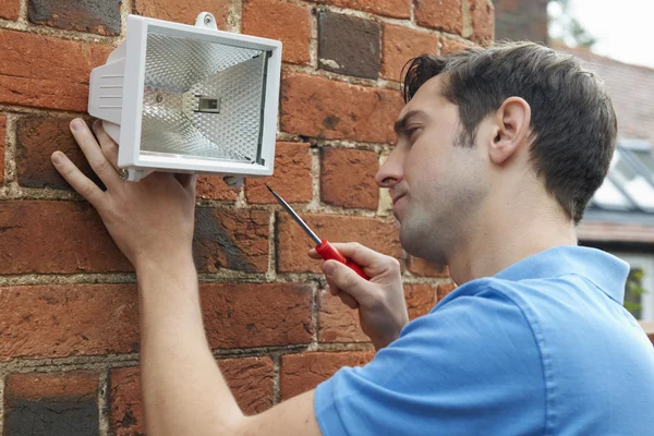 Uomo che misura la luce di sicurezza alla parete della casa — Foto Stock