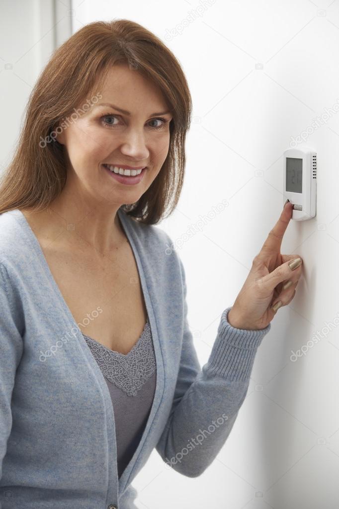 Smiling Woman Adjusting Thermostat On Home Heating System