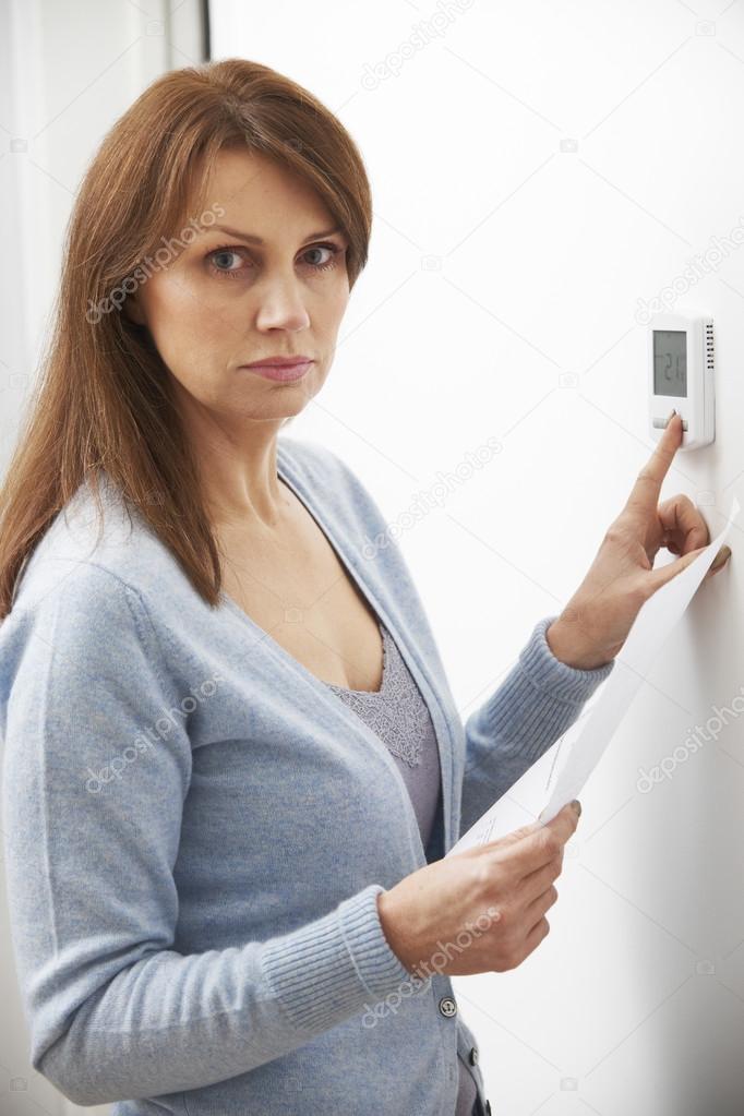 Worried Woman With Heating Bill Turning Down Thermostat