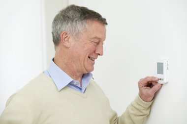 Senior Man Adjusting Central Heating Thermostat clipart