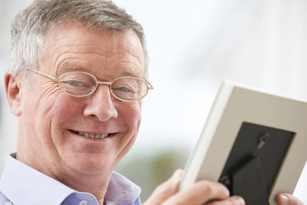 Usměvavá starší muž při pohledu na fotografii v rámečku — Stock fotografie