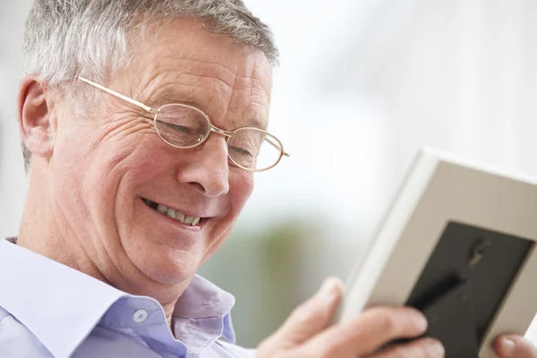 Hombre mayor sonriente mirando la fotografía en el marco —  Fotos de Stock