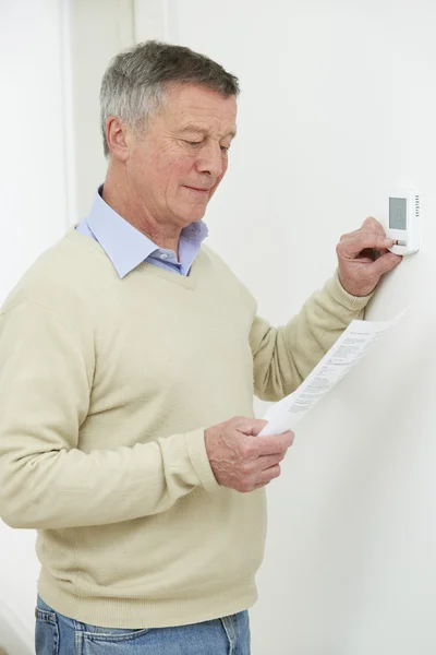 Worried Senior Man Turning Down Central Heating Thermostat — Stock Photo, Image