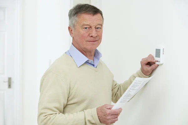 Homme âgé inquiet avec Bill désactivant le thermostat de chauffage — Photo