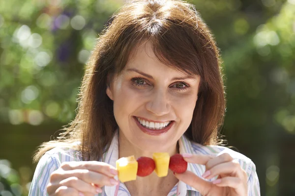 Middle Aged Woman Eating Fruit Kebab In Garden — Stock Photo, Image