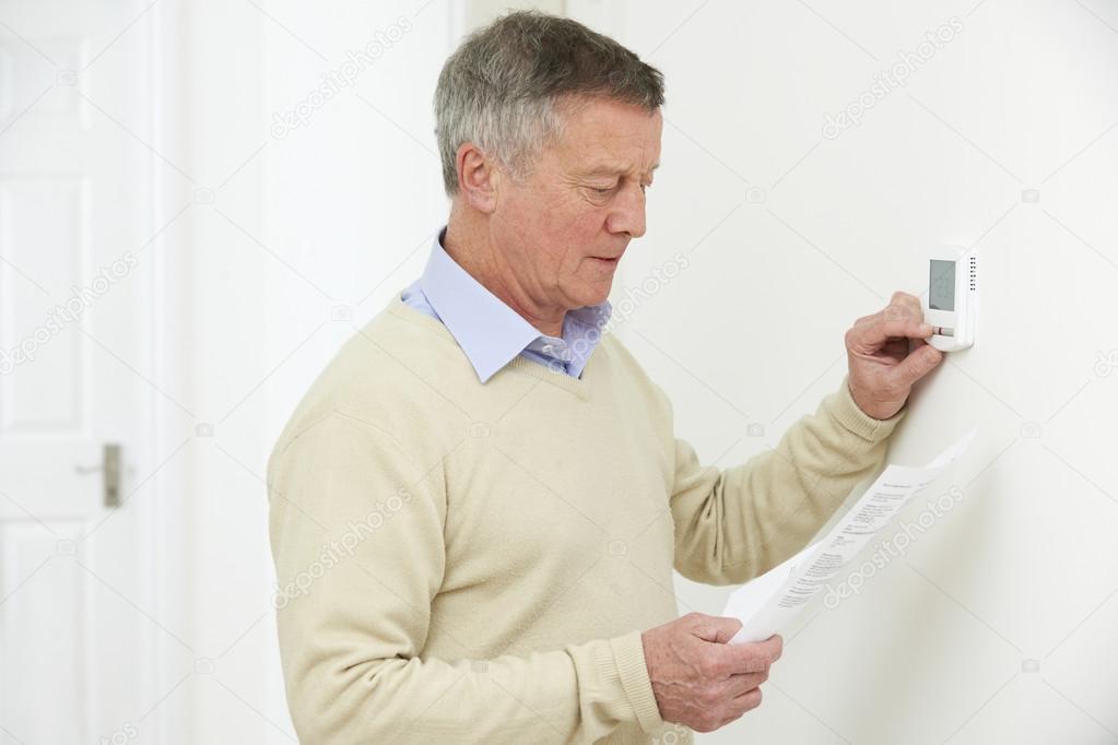 Worried Senior Man With Bill Turning Down Heating Thermostat