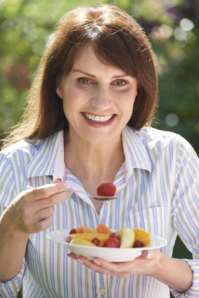 Mittelalte Frau isst Schale mit Obst im Garten — Stockfoto