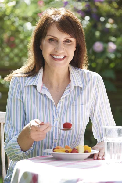 Mujer de mediana edad comiendo tazón de fruta en el jardín —  Fotos de Stock