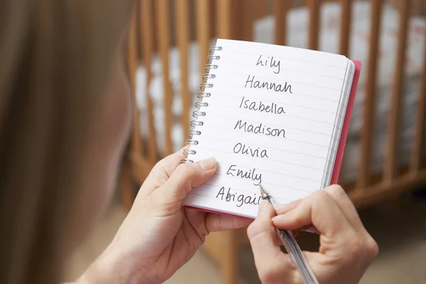 Mujer escribiendo posibles nombres para bebé niña en guardería — Foto de Stock