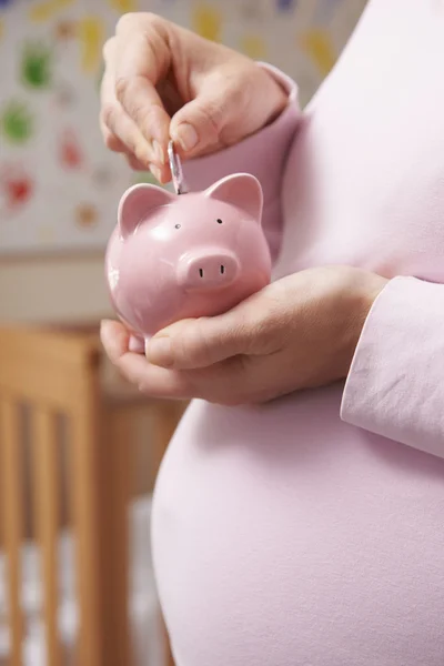 Zwangere vrouw In kwekerij geld steken in Piggy Bank — Stockfoto