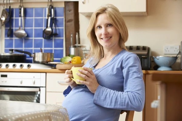 Embarazada mujer relajante en cocina con taza de té —  Fotos de Stock