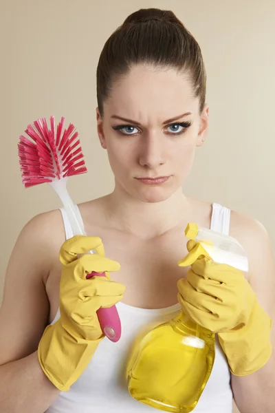 Mujer joven sosteniendo productos de limpieza buscando infeliz —  Fotos de Stock