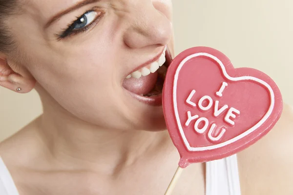 Rozzlobený mladá žena kousání srdce ve tvaru "Miluji tě" lízátko — Stock fotografie