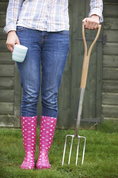 Žena v růžové gumáky hospodářství zahrada vidlice a pohár — Stock fotografie