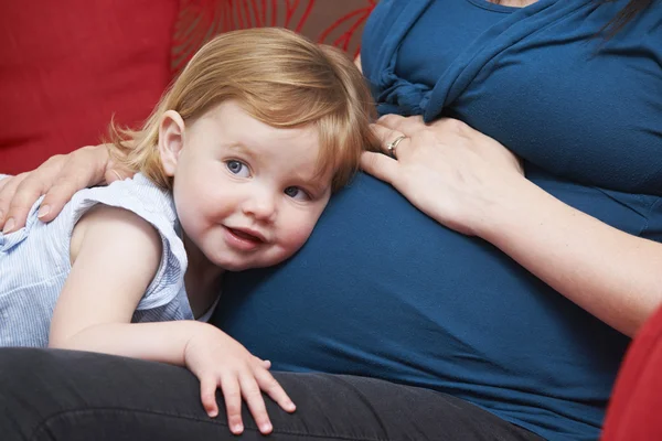 Chica joven escuchando la barriga de la madre embarazada — Foto de Stock