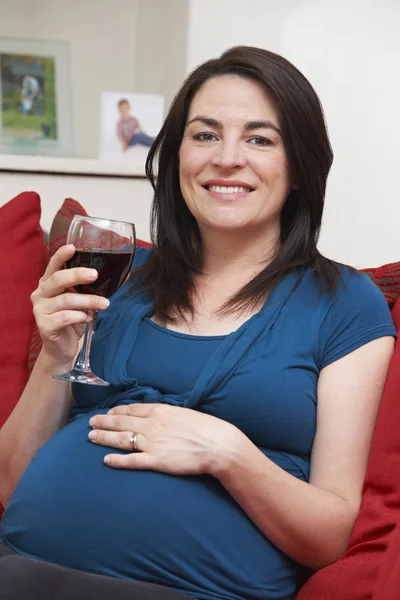 Sorridente donna incinta bere un bicchiere di vino a casa — Foto Stock