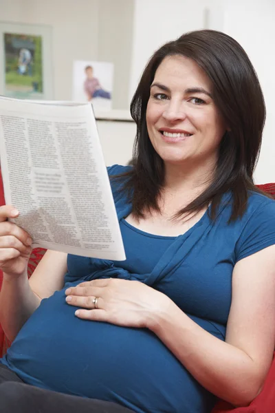 Hamile kadın kanepe okuma dergi üzerinde oturuyordu — Stok fotoğraf