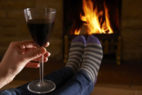 Женщина со стеклом красного вина расслабляется у огня — стоковое фото