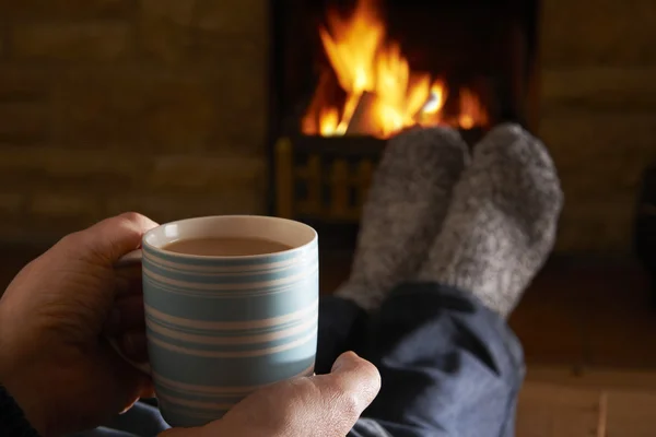 Homem com bebida quente relaxante pelo fogo — Fotografia de Stock