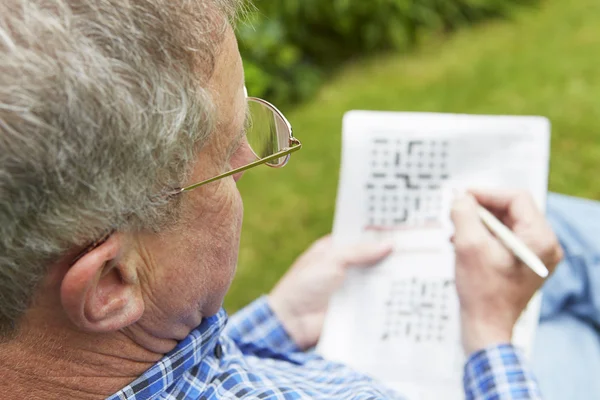 Старший человек делает кроссворд головоломки в саду — стоковое фото