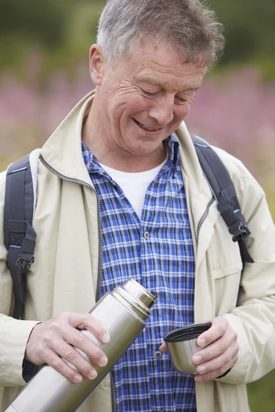 Senior Man gieten hete drank uit kolf op wandeling — Stockfoto