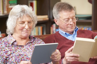 Senior Couple Using Digital Tablet And Reading Book clipart