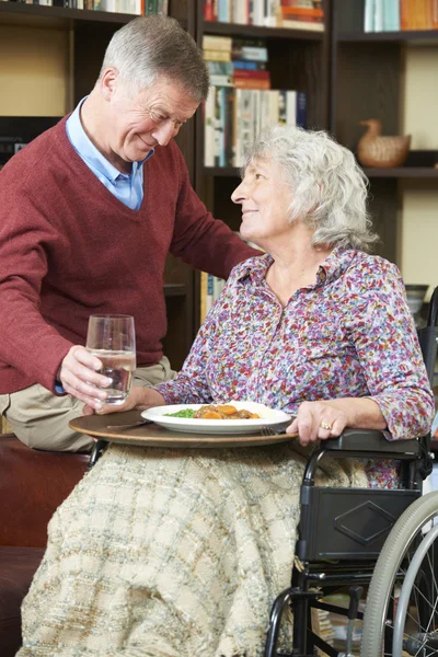 Hombre mayor sirviendo esposa en silla de ruedas con comida — Foto de Stock