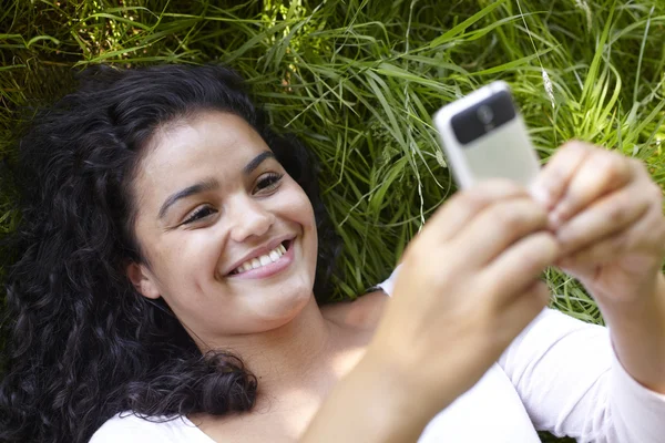 Молода жінка лежить траві використовуючи мобільний телефон — стокове фото