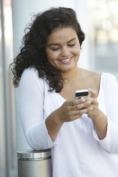 Молодая женщина читает текстовое сообщение в городских настройках — стоковое фото