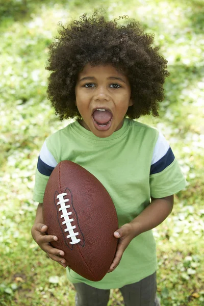 Збуджений молодий хлопчик грає американського футболу в парку — стокове фото
