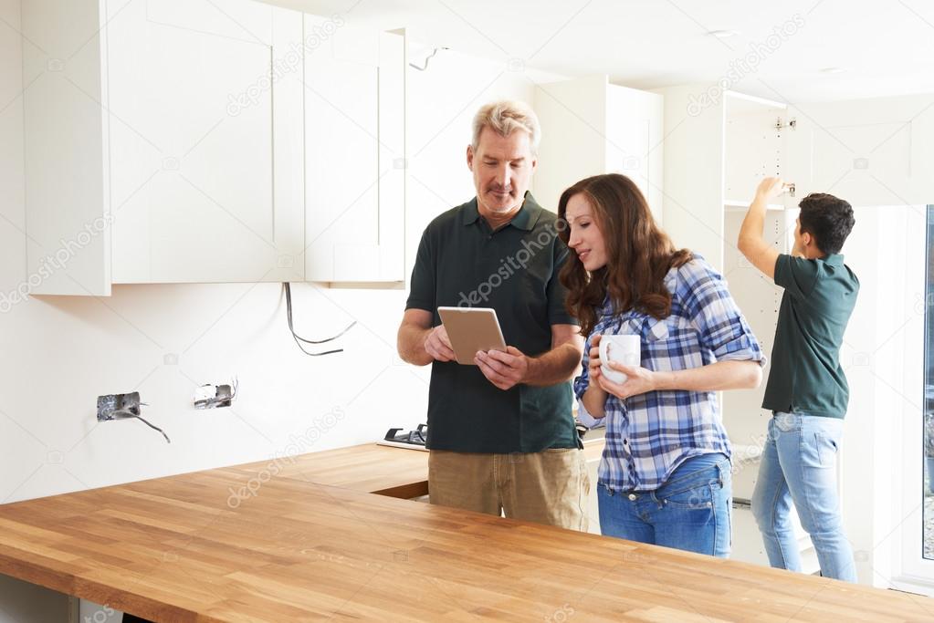 Woman With Carpenter Looking At Plans For Kitchen On Digital Tab