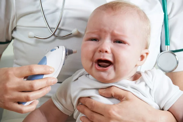 Медсестра измеряет температуру плачущего ребенка с помощью цифрового термометра — стоковое фото