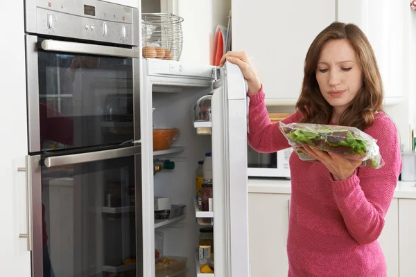 Mulher que verifica a venda pela data no saco da salada no refrigerador — Fotografia de Stock